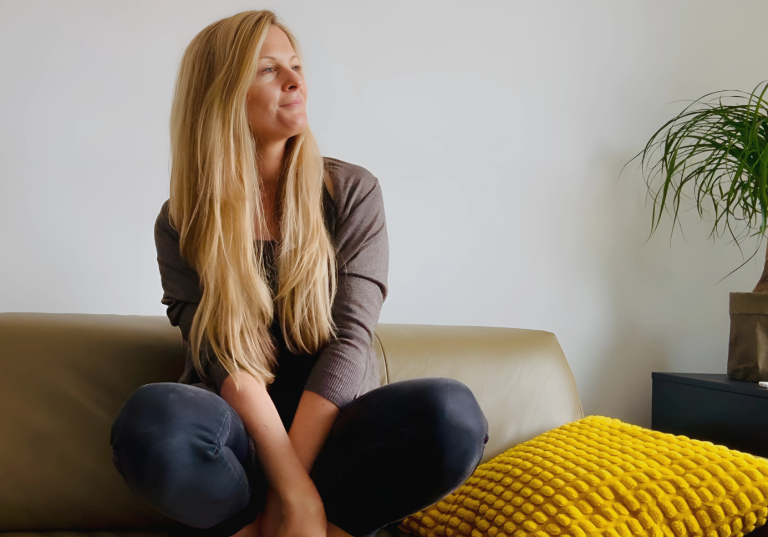 Frau mit langen Haaren sitzt auf einem Sofa und schaut erfüllt zur Seite.